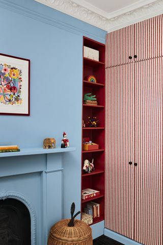 baby boy nursery with blue walls and red storage alcove, red and white stripe wardrobe doors, basket, artwork , toys