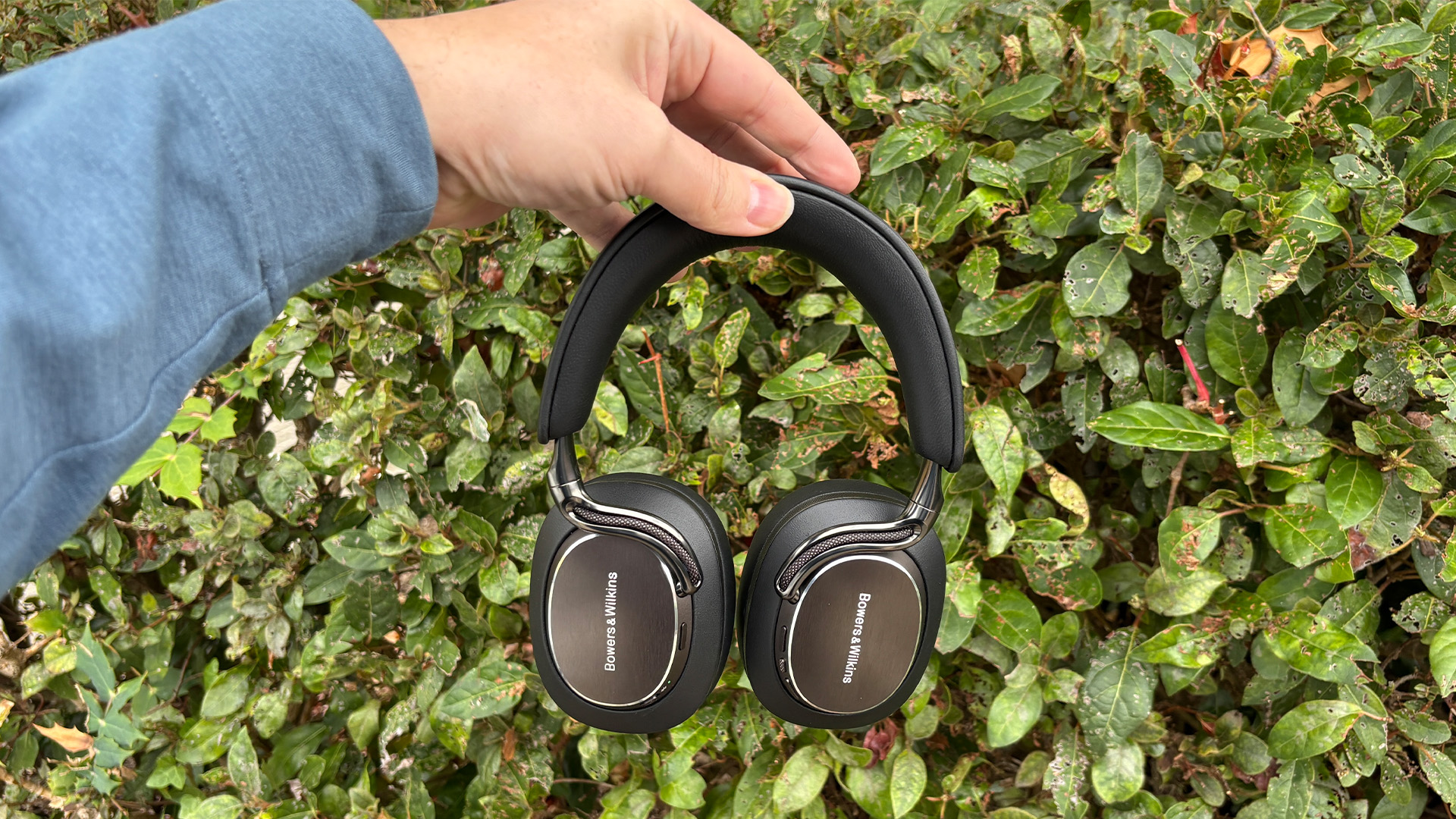 Bowers &amp;amp; Wilkins Px8 S2 wireless headphones held in hand in front of bush
