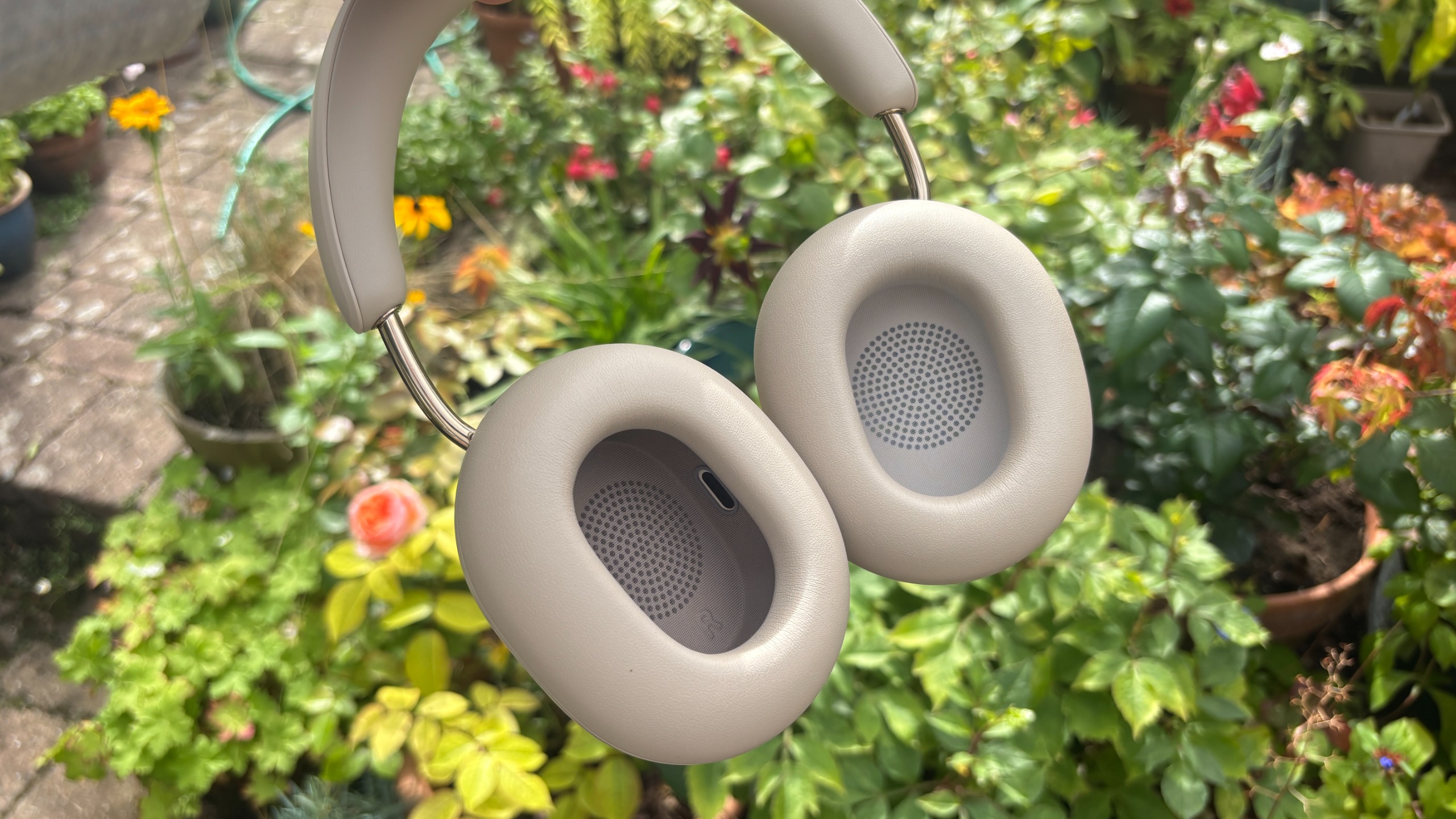 Sonos Ace Ultra wireless headphones held up in hand against plants, showing inside of earcups