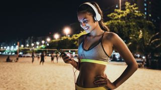Should you exercise before you sleep? Image shows jogger at night using her smartphone and stopping to stand and rest on beach
