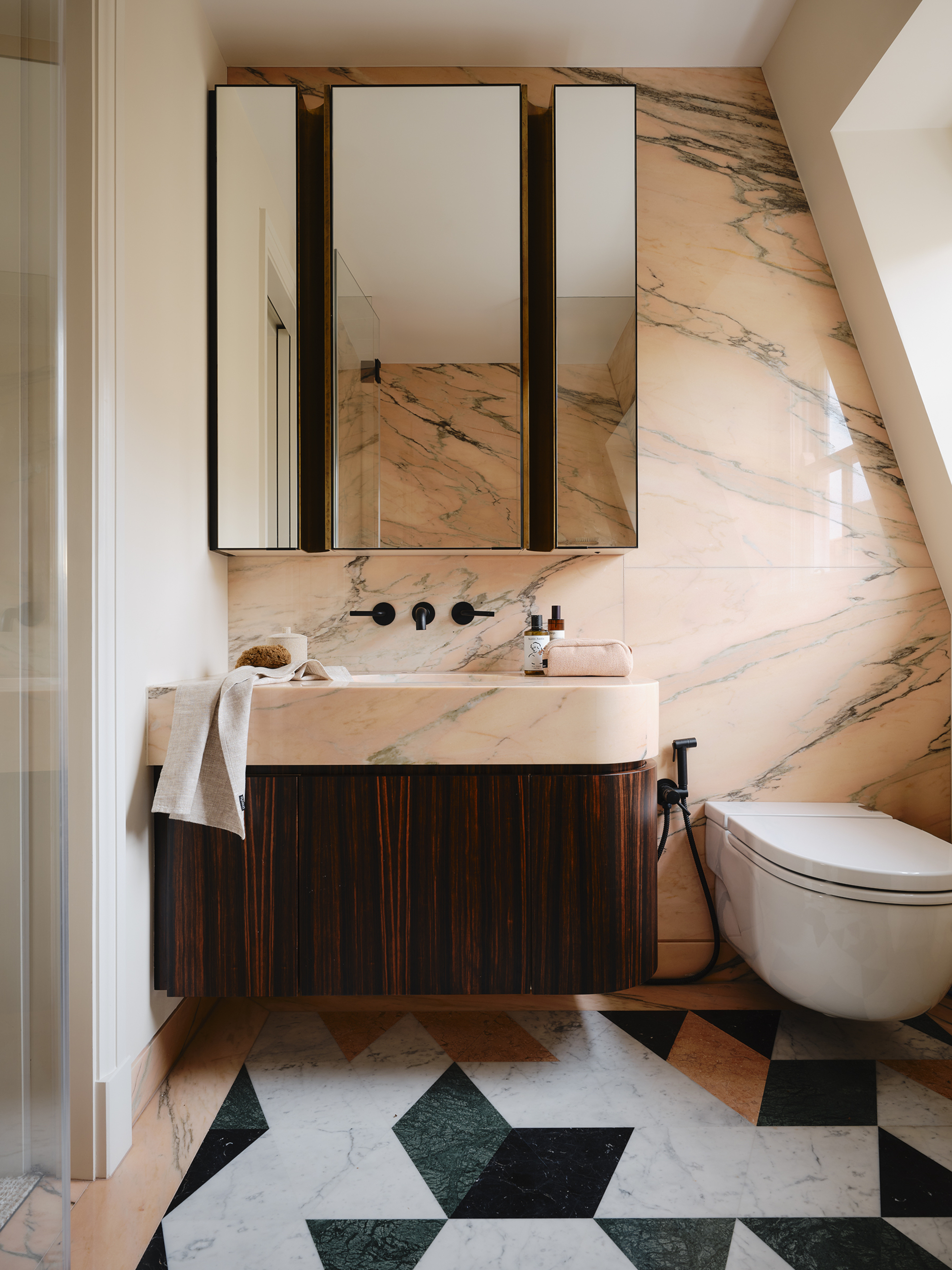 marble bathroom with peach-stone walls, mirrored medicine cabinet, floating vanity with fluted timber details, and green and white marble floor