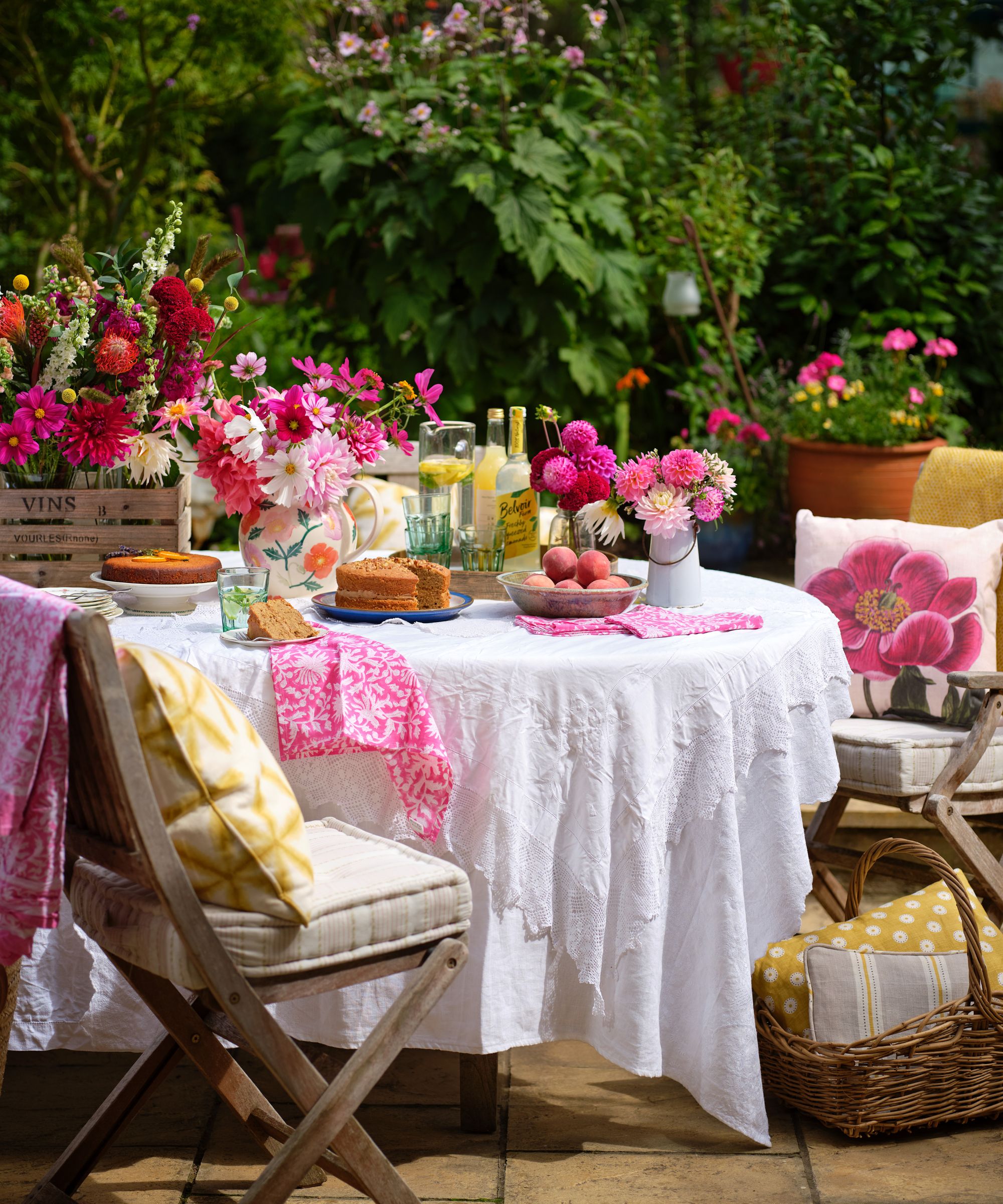 Summer garden table styled with white tablecloths and vases of hot summer flowers including dahlias and cosmos in pinks, reds and orange