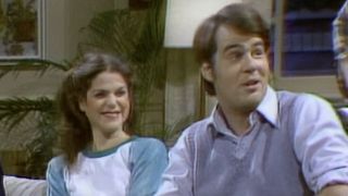 Gilda Radner and Dan Aykroyd sitting on a couch during "Loud Family" SNL sketch in 1978.