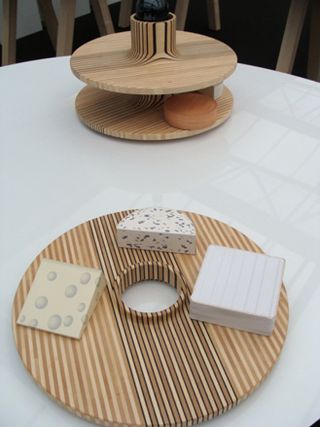 A circular cheese board with three cheeses in front of a multi levelled circular storage device.