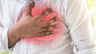 We see the chest of a man in a work shirt. He is clutching his heart in an area digitally highlighted in red to show he is having a heart attack.