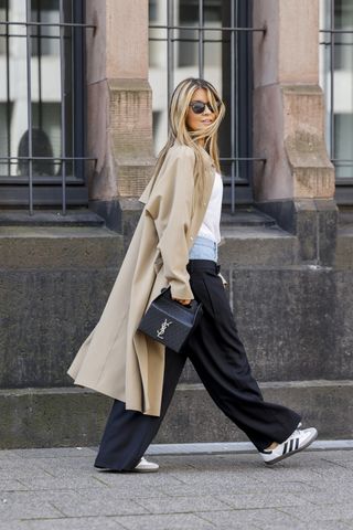 DUSSELDORF, GERMANY - SEPTEMBER 12: Gitta Banko, wearing a white shirt by gitta Banko, a beige coat by Herno, blue pants with jeans waist (pant in pant) by Dion Lee, white sneakers Samba by Adidas, a black bag by Saint Laurent and sunglasses by Izipizi, during a streetstyle shooting on September 12, 2023 in Dusseldorf, Germany. (Photo by Streetstyleshooters/Getty Images)