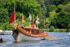 Gilded and glittering under her array of flags, Gloriana responds to her rowers as she glides up the Thames at Petersham.