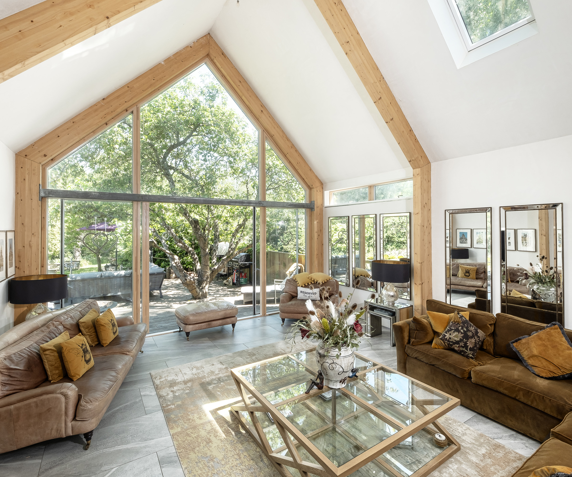 A large living area with architectural glazing allowing plenty of natural light into the space. The glazing contains sliding doors which are open out onto a patio