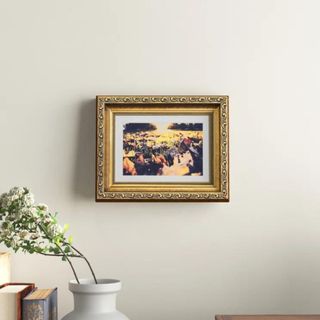 A gold engraved picture frame hangining on a white wall