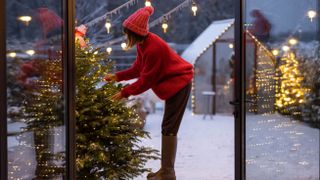 A woman in red decorating a Christmas tree outdoors