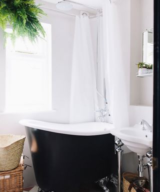 White bathroom with black painted bath, patterned floor tiles and a fern hanging from the shower reel