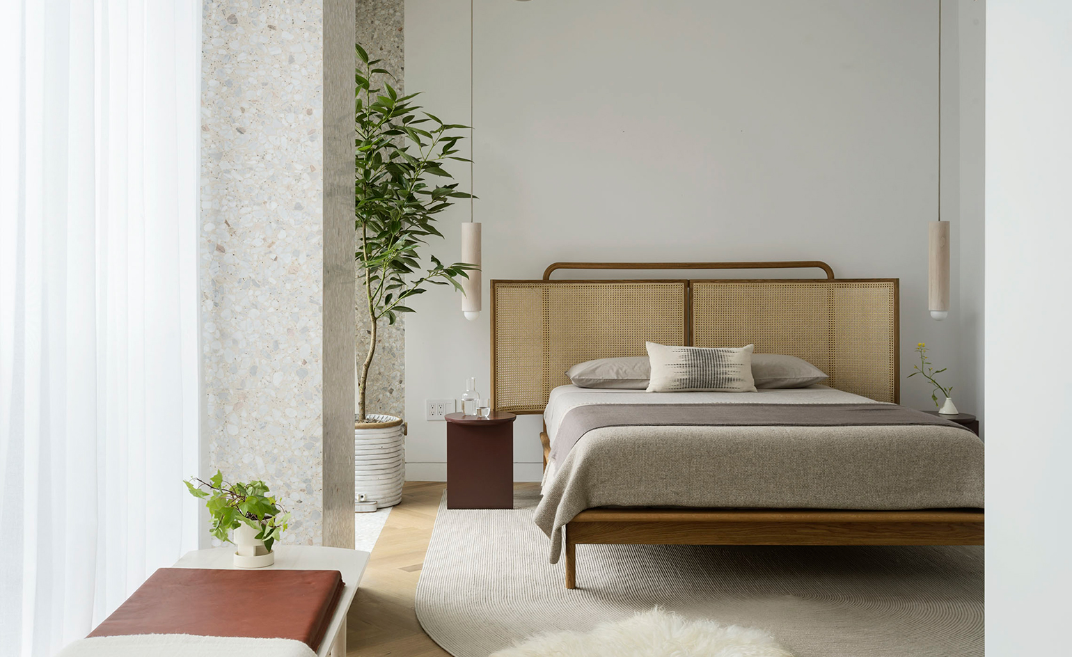 A photo of a double bed (wooden frame) in the centre of the room with grey linen and a cane head board. Can side tables on either side.
