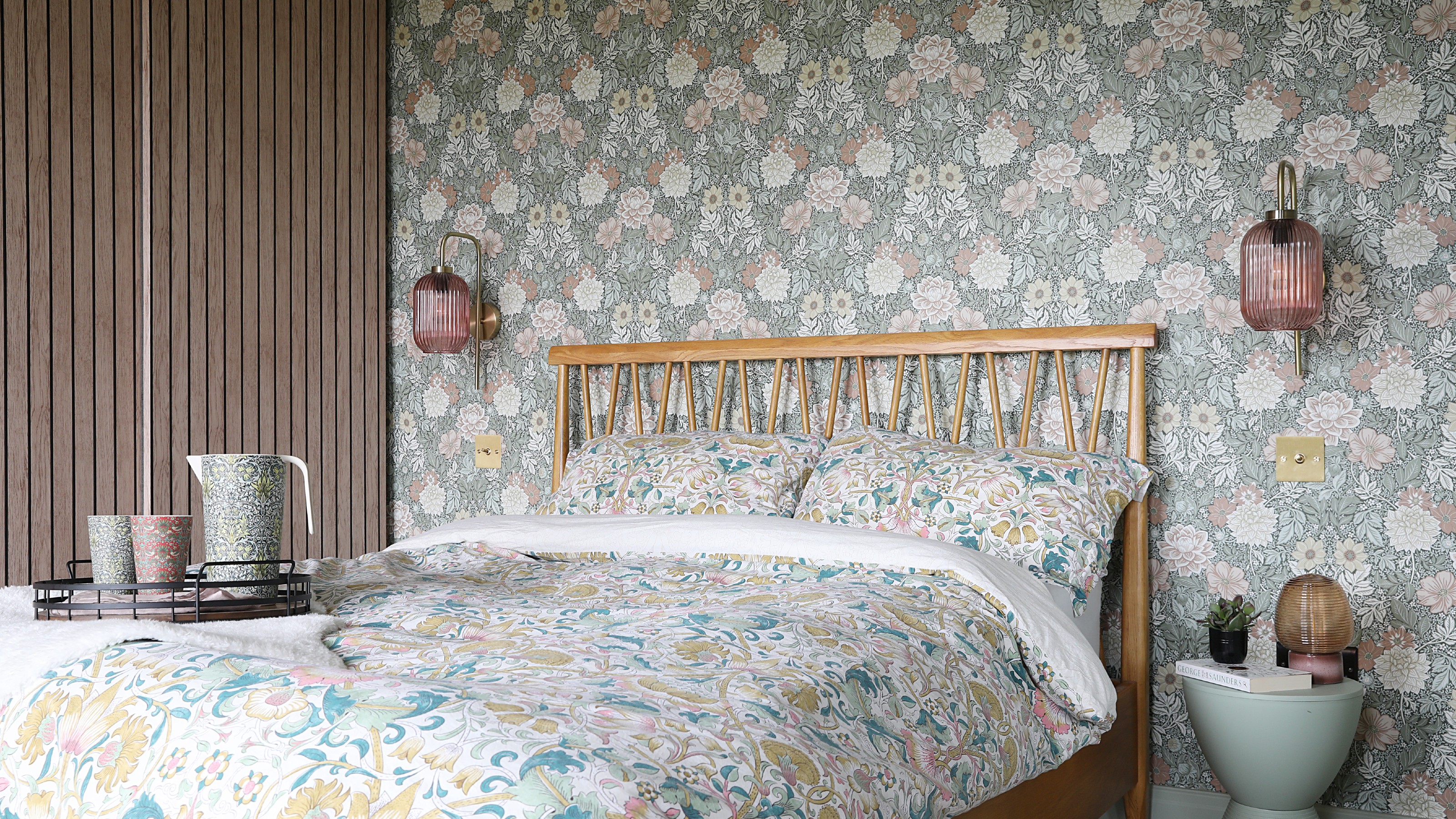 A bedroom with a feature wall behind the bed covered in a floral Morris & Co wallpaper and coordinating Morris & Co bed linen covering the bed