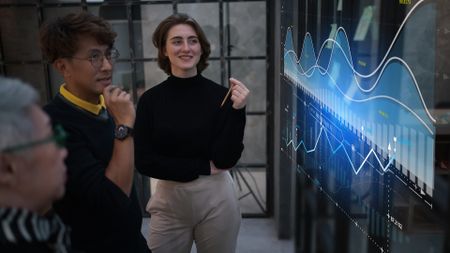 Businesspeople stood in front of a large screen showing a glowing blue graph, to represent SME digital transformation.
