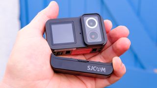 A photo of the SJCAM Sj20 being held up with the lenses and removable battery showing against a blue backdrop.