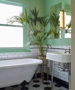 bathroom with mint green upper wall, white subway tiles on lower half of wall and white sink and bath with large houseplant