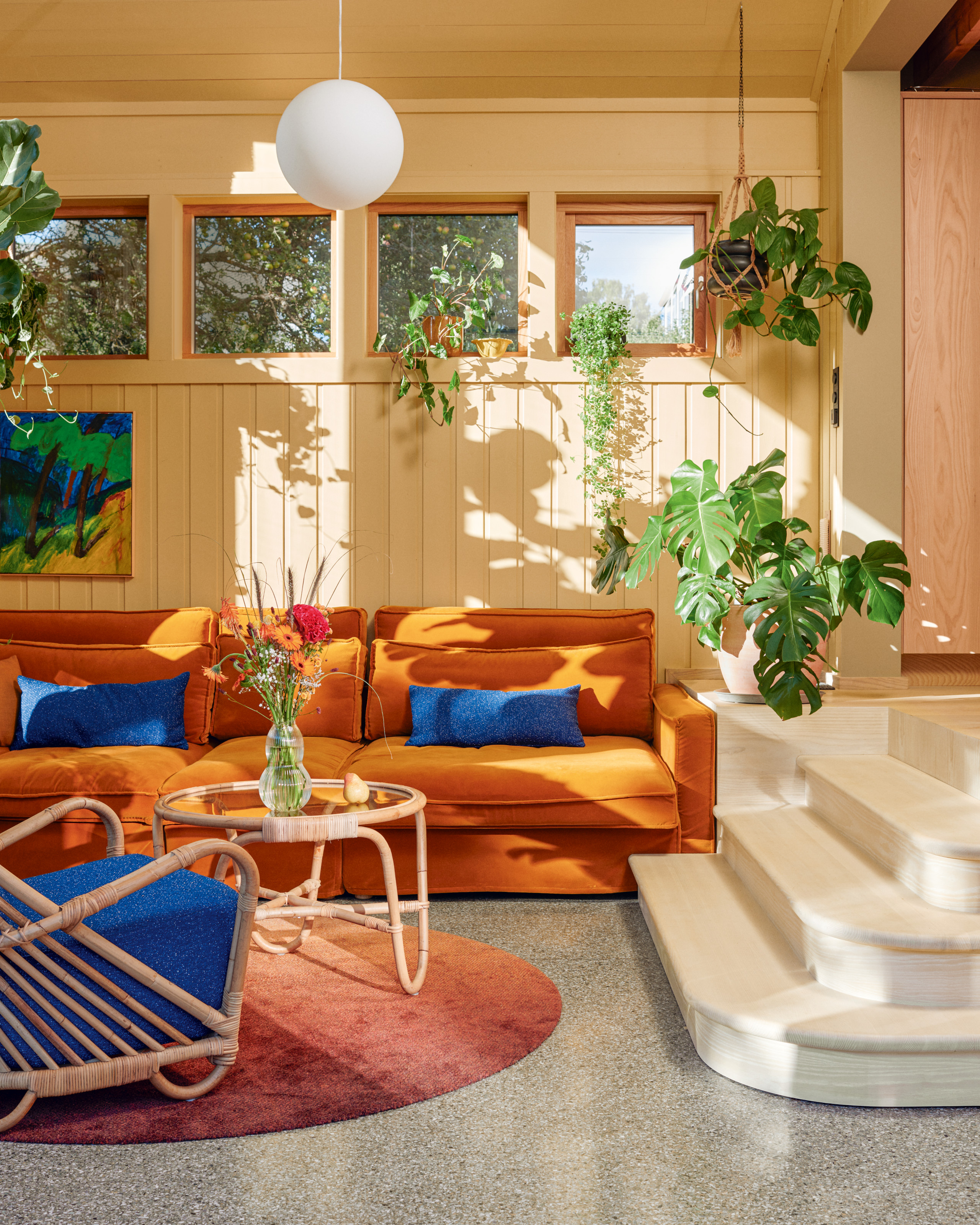 Sunken living area with grey terrazzo floor, orange sofa, blue and wicker armchair, rattan coffee table and single globe pendant light
