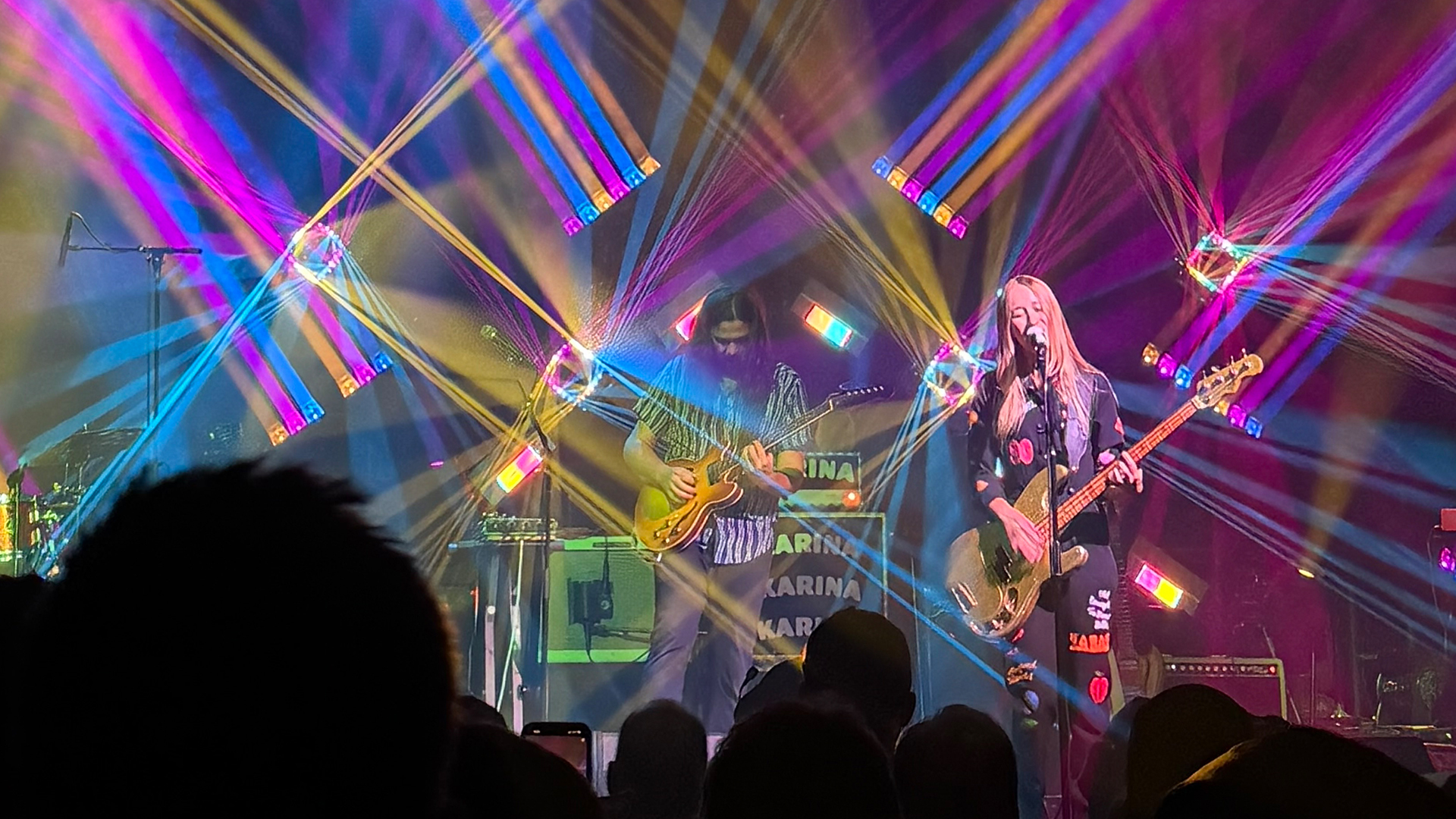 a rock band on stage in a crowded night club full of multicolored lights