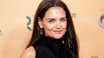 Katie Holmes in front of a plain backdrop on a red carpet