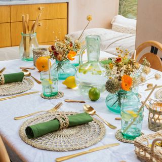 White table with rattan placemats, blue glasses and gold cutlery