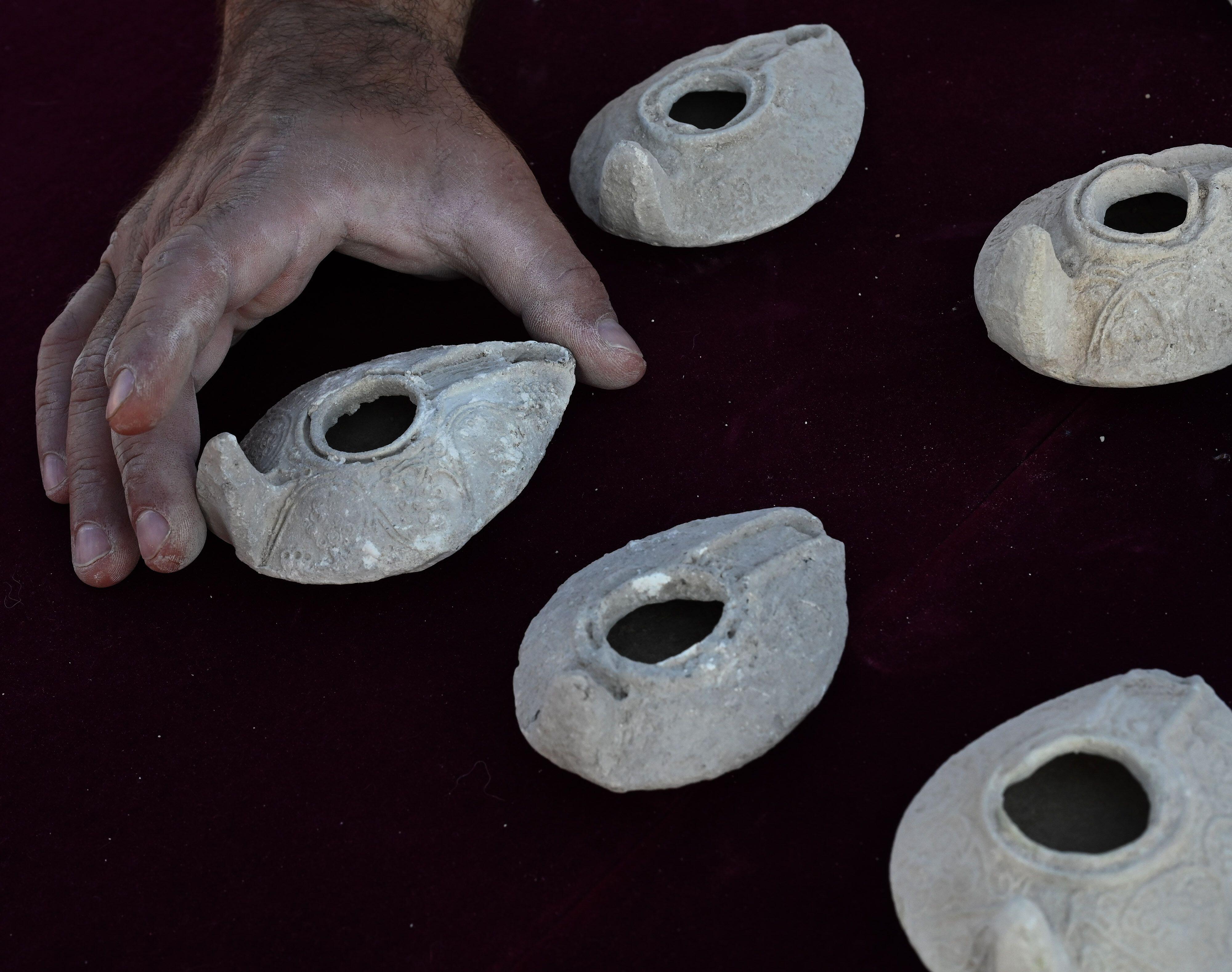 An archeologist from The Israel Antiquities Authority holds a clay lamp from the eighth and ninth centuries CE, unearthed in the courtyard of an elaborate 2,000 year old Second Temple Period family burial cave, known as the Salome Cave, in the Lachish Forest in the Judean lowlands.