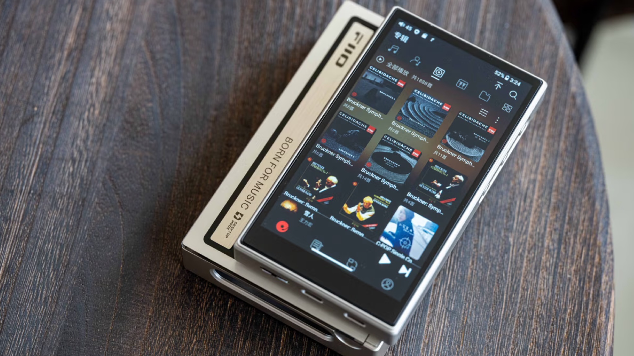 FiiO M21 music player lifestyle shot on a round wooden table with the screen active and showing icons for music tracks