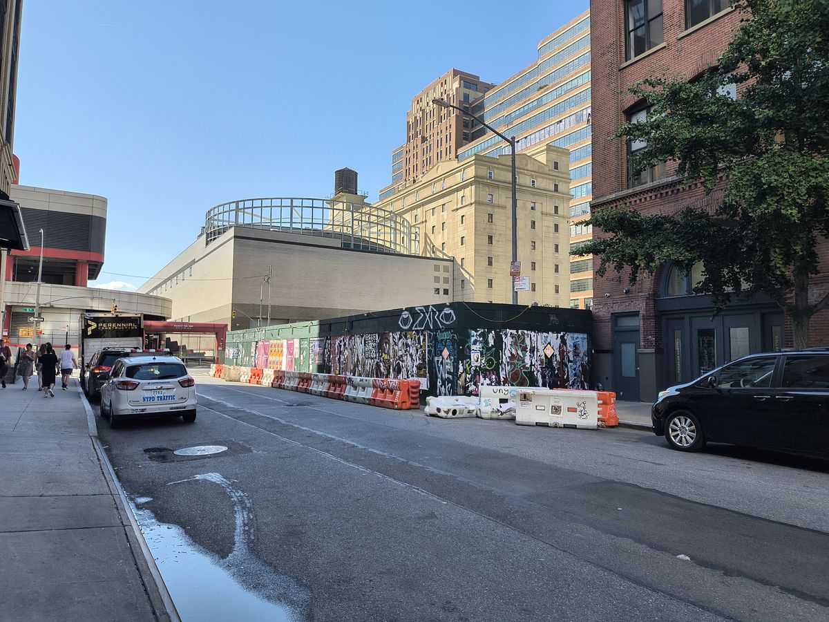 Urban street showing cars parked on either side before a set of construction barriers in the shade on a sunny day