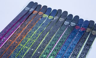 Seven branded pairs of Black Crown skis. Each ski features the Black Crows logo with a logo based on a bird-like shape at the top of each ski. Each ski is black with a varied neon colour design.