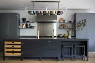 Black painted kitchen cabinets with dark gray pantry, chrome cooker and backsplash and statement lighting.