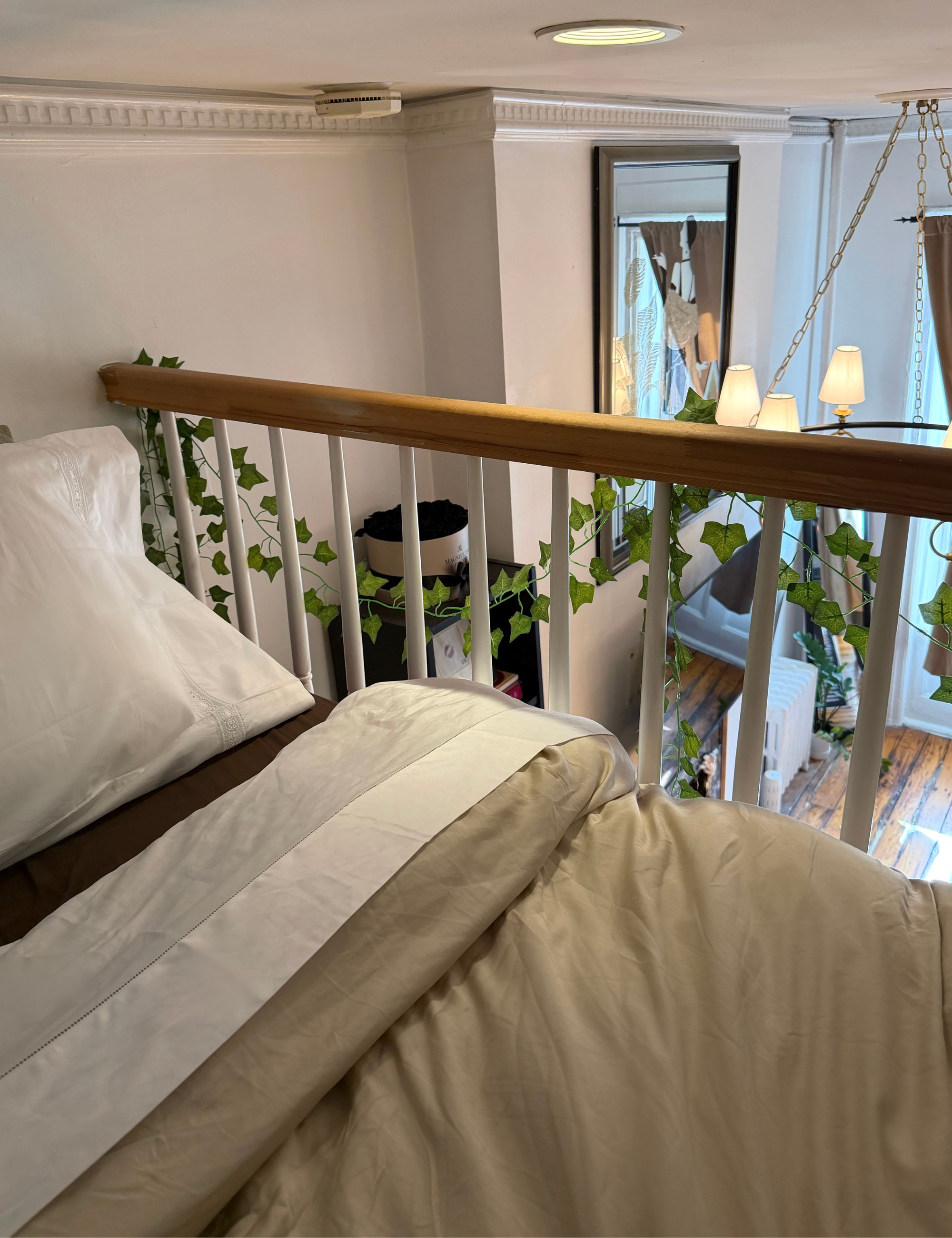 Lofted NYC bed setup featuring white Sferra Giza 45 Sateen bed sheets that overlooks a charming living room area with large windows