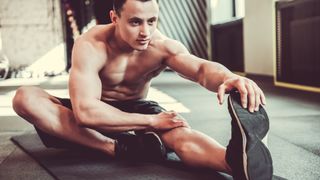 Man stretching his left hamstring while sitting down during workout