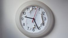 A white analog clock hangs on the wall with its background ripped up