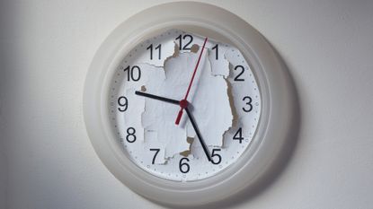 A white analog clock hangs on the wall with its background ripped up