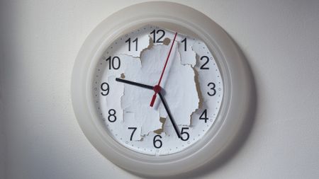 A white analog clock hangs on the wall with its background ripped up