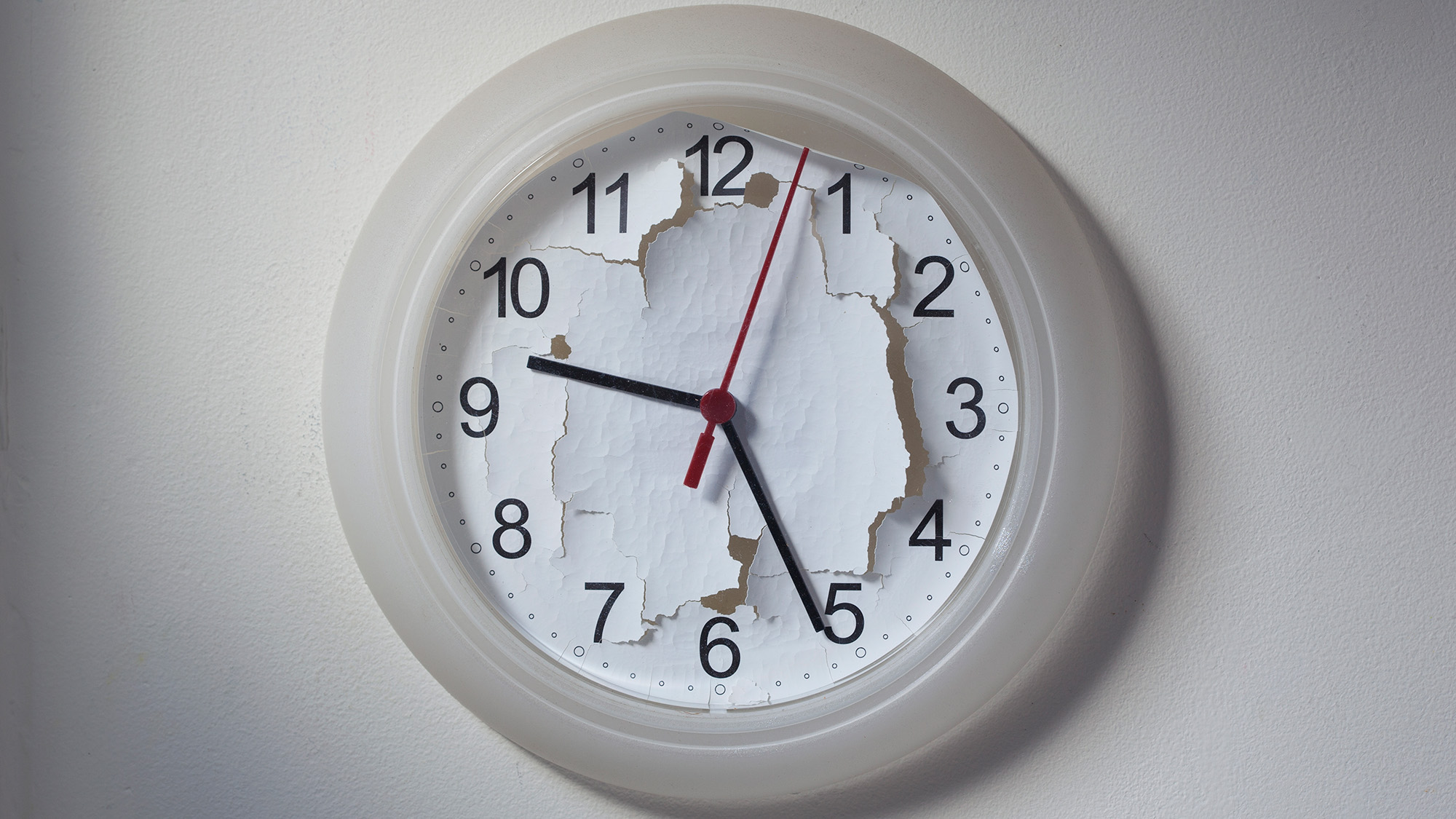 A white analog clock hangs on the wall with its background ripped up
