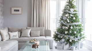 Gray living room with Christmas tree decorated in silver in the perfcet position away from the fireplace to demonstrate how to keep a Christmas tree alive