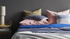 A pile of multicoloured bedding on a bed in a bedroom with a dark painted wall