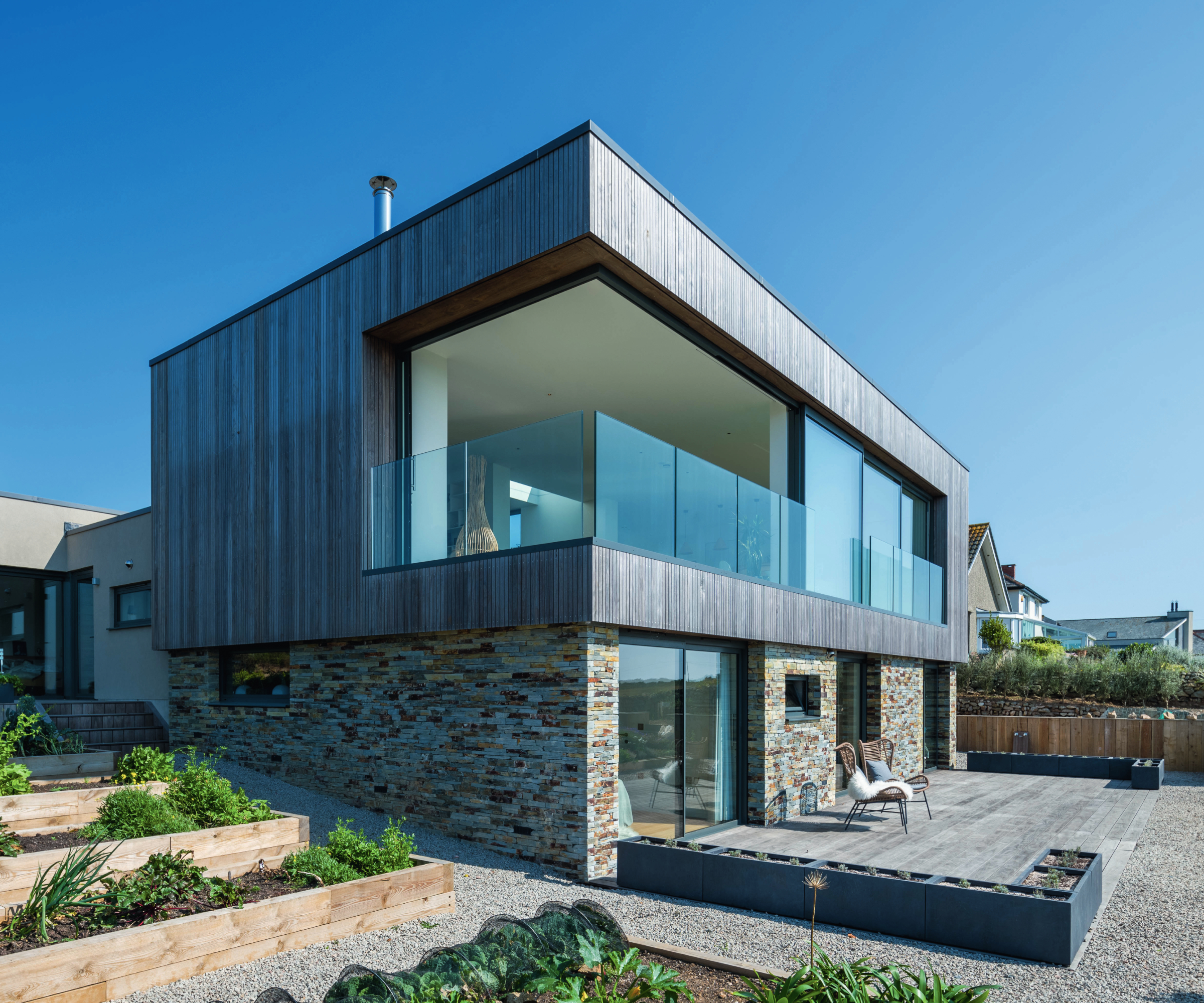 modern house with corner wraparound glazing on first floor, glass balcony and sliding patio doors above and on ground floor below