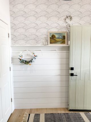 Accent wall with white shiplap patterned wallpaper and wreath held on pegs