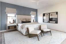 A bedroom with a blue accent wall, windows flanking the bed's headboard, and blinds pulled half way down the windows
