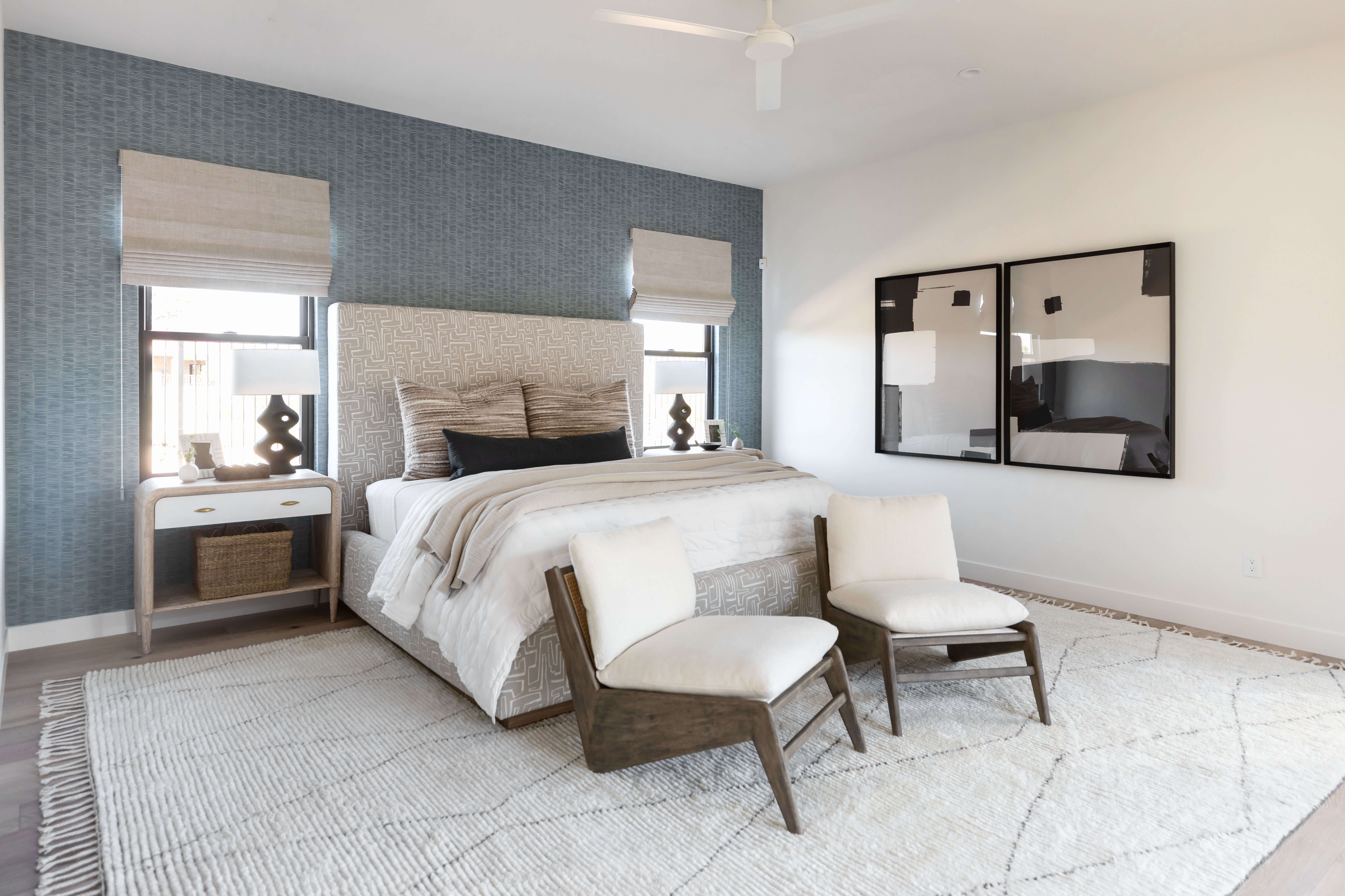 A bedroom with a blue accent wall, windows flanking the bed&#039;s headboard, and blinds pulled half way down the windows