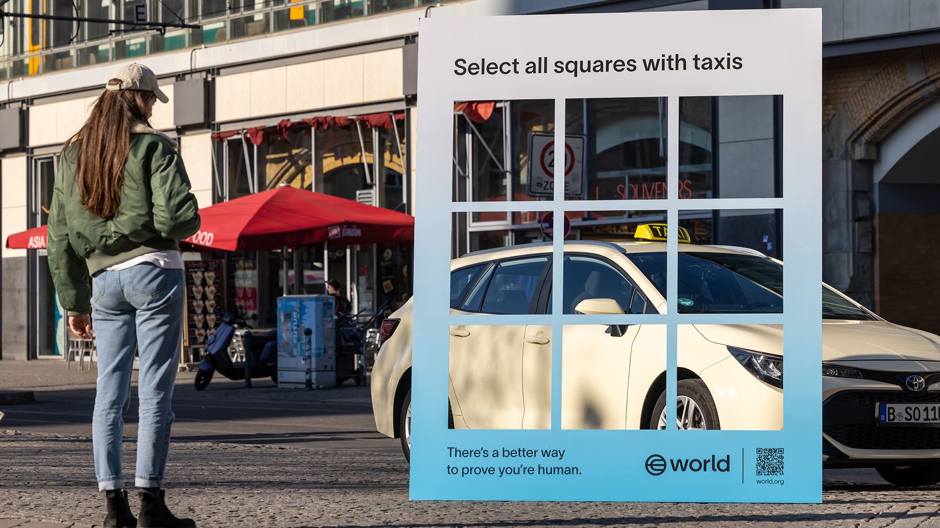 A woman stands next to a rectangle in front of a white car.