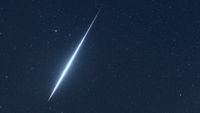 A blue meteor is photographed streaking through a dark night sky dotted with faint stars.