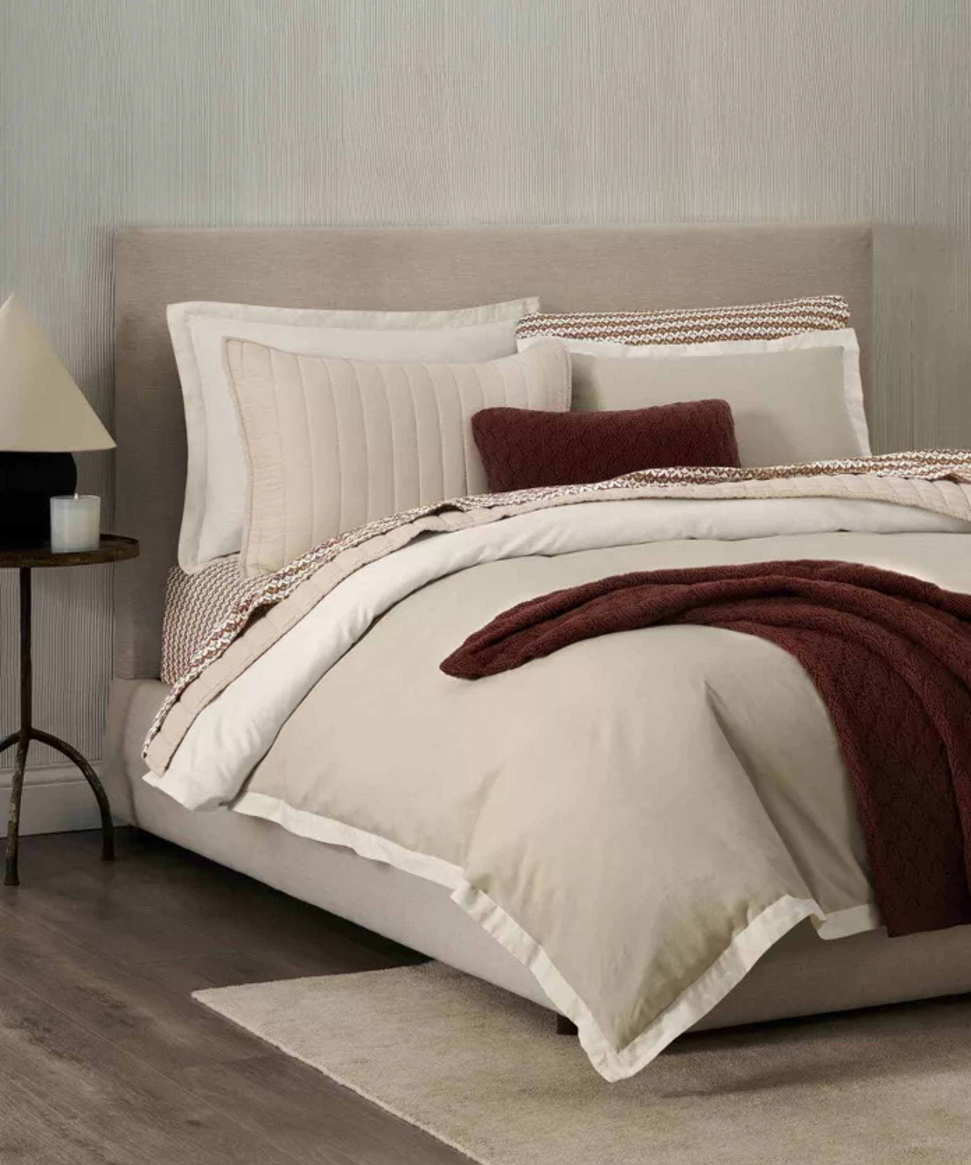 a bed with a soft tan duvet cover, a dark brown blanket and accent pillow, and other pillows on top of the bed