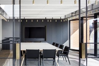 View of the boardroom at Dunhill's HQ featuring a large table with a white top, black chairs, dark coloured wall panels, a large screen, multiple lights and tall glass doors that lead to the outdoor terrace