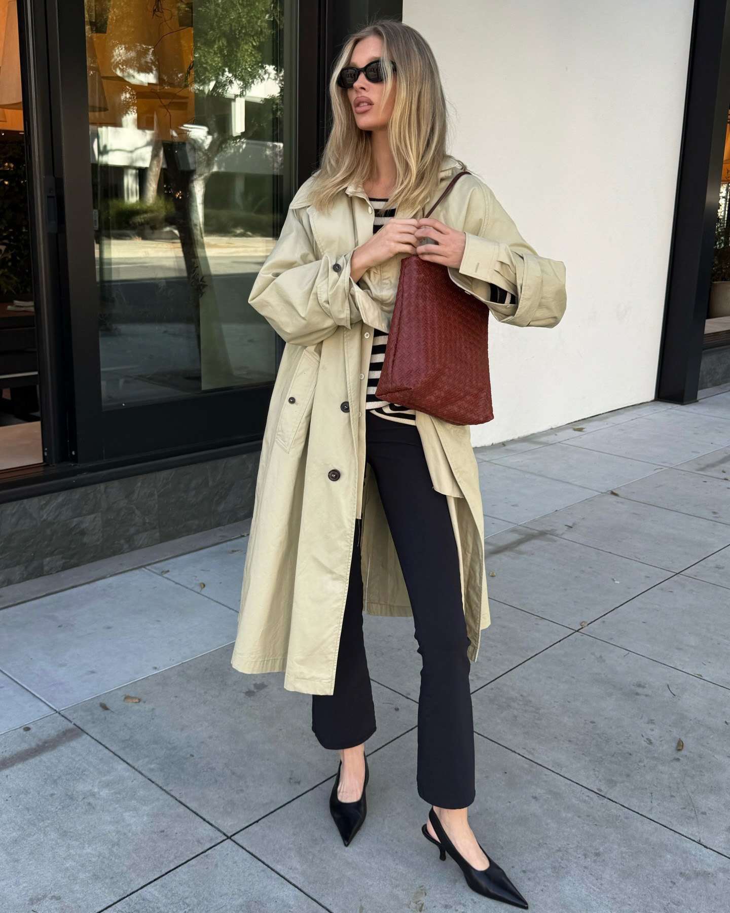Elsa Hosk wearing a trench coat, striped shirt, cropped flare pants, and kitten-heel slingback shoes