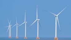A series of white wind turbines sit in the ocean.
