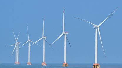 A series of white wind turbines sit in the ocean.