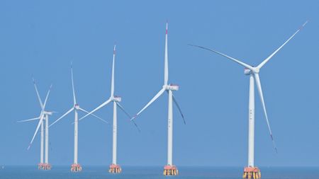 A series of white wind turbines sit in the ocean.
