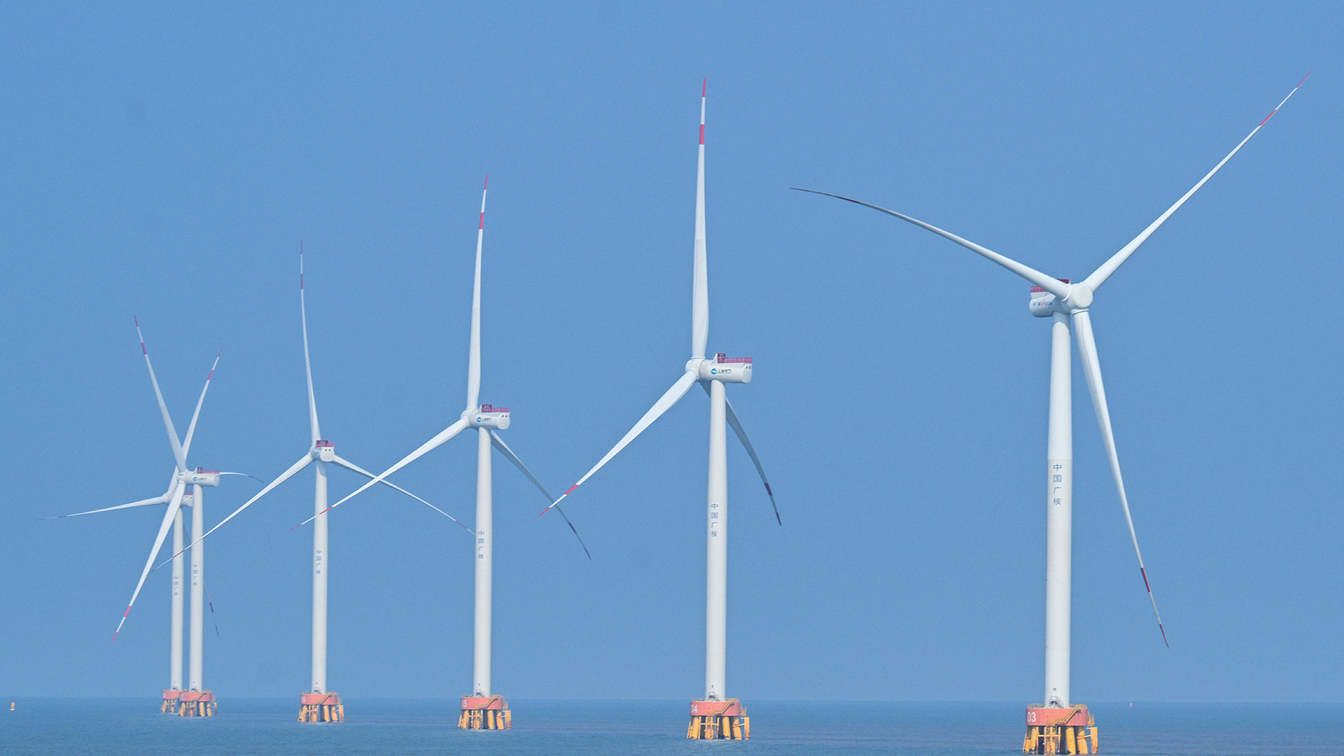 A series of white wind turbines sit in the ocean.